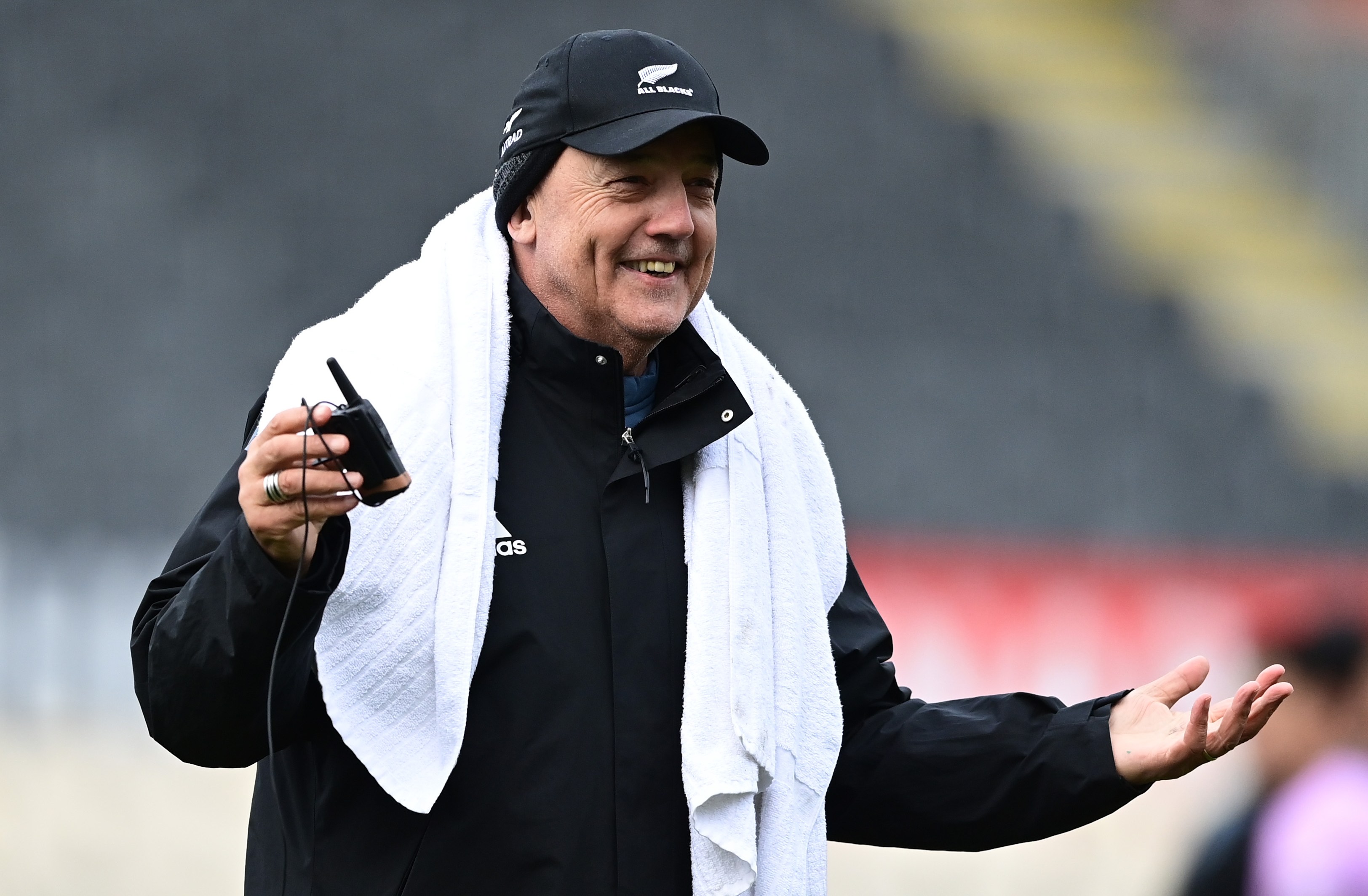 Mental skills coach Gilbert Enoka smiling with a towel over his shoulder, holding a walkie-talkie.