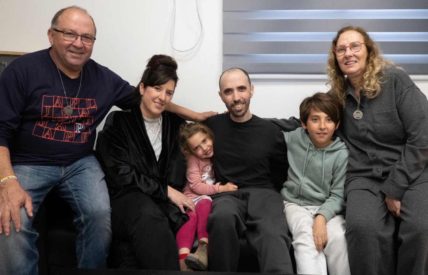The Tal Shoham family sitting together on a couch, from left to right: an older man, a woman, a young girl, a man, a boy, and an older woman.