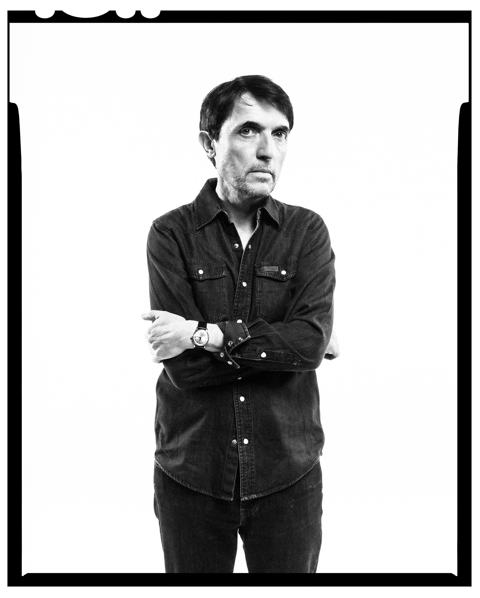 Black and white portrait of Radiohead's Alex Lake, wearing a denim shirt and jeans, with his arms crossed.