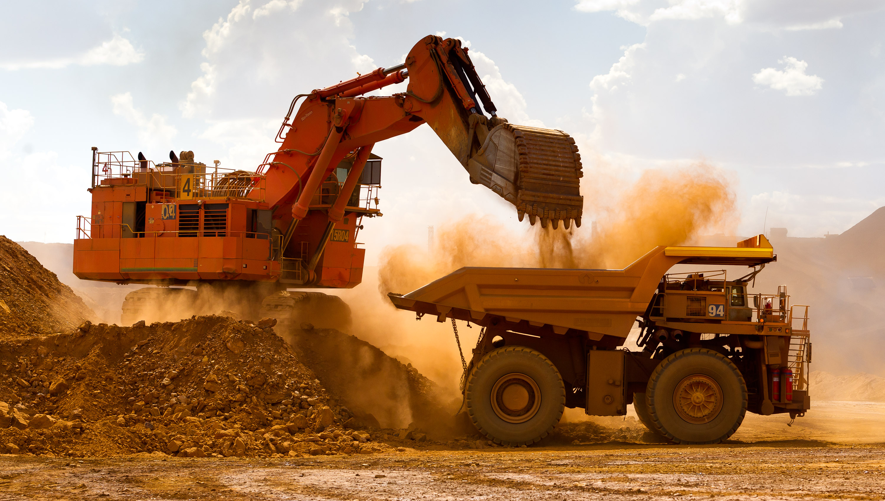 A large orange digger loading material into a haul truck at the Rio Tinto Group's West Angelas iron ore mine in Pilbara, Australia.