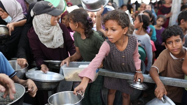 children and women hold empty pots as they wait for food