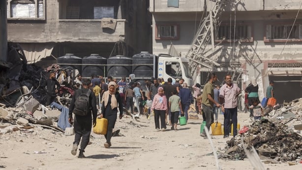 People move along dusty roads beside damaged buildings in Gaza