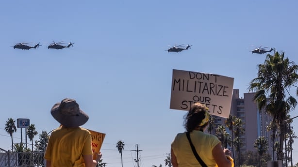OCEANSIDE, CALIFORNIA - OCTOBER 18: Protesters hold signs of No Kings in America at the main entrance of the Marine Corps Base Camp Pendleton while US Marine Helicopters fly over on October 18, 2025 in Oceanside, California. A 17-mile stretch of the 5 Freeway was temporarily closed on Saturday due t