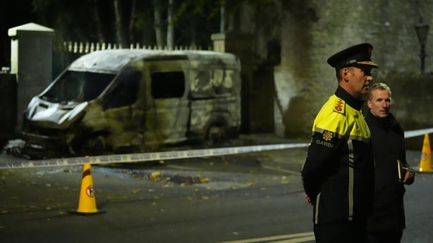 Garda Commissioner Justin Kelly in the foreground with a burnt out van in the background