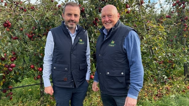 Two men in gillets beside apple trees