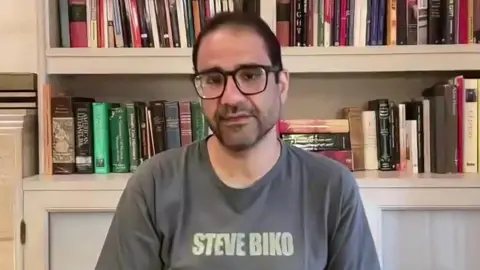 BBC Alaa Abdel Fattah speaks via video link to the BBC, sitting in front of a bookshelf and wearing a grey t-shirt with the words Steve Biko on it
