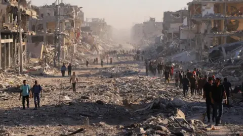 Reuters A scene of a street of completely and partially destroyed buildings with people walking along the rubble