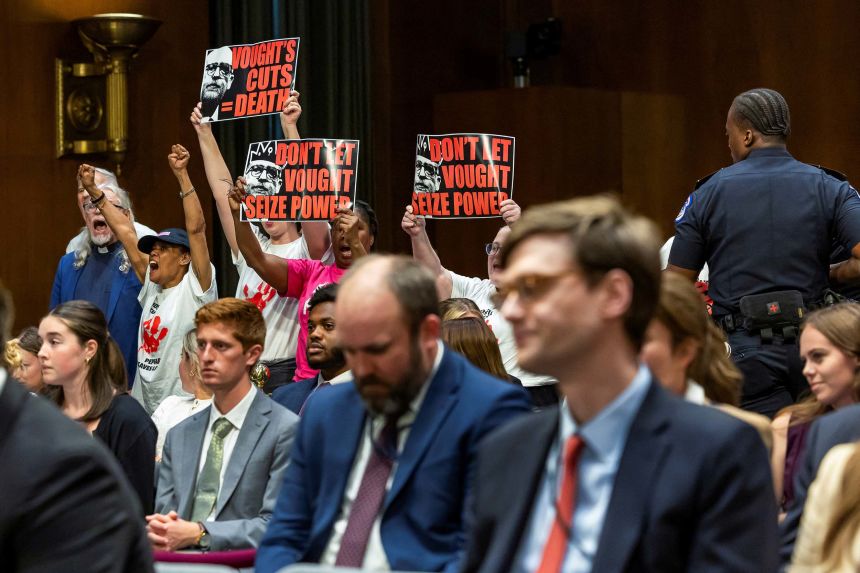 Activists protest the Russ Vought as he testifies before the Senate Committee on Appropriations on June 25.