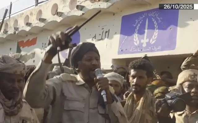A man shouting into a microphone surrounded by other men