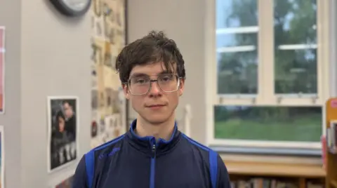 Patrick, with blue tracksuit top and glasses, in front of window at Mercy College in north Belfast