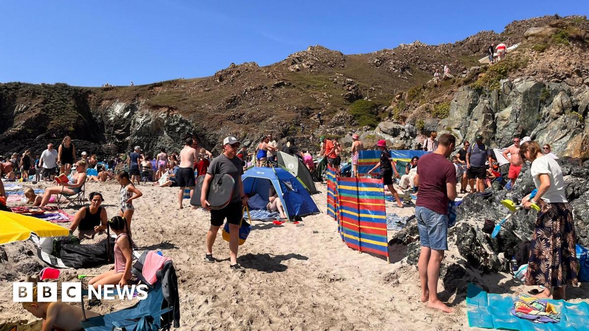 A beach with lots of people and wind breaks, with cliffs behind and blue sea