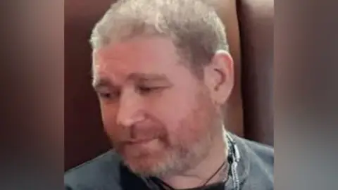 Family photo Richard Sanders wearing a black T-shirt. He is looking down to his left, towards the ground