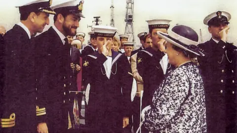 Roly Woods Commander Woods and other personnel onboard HMS Lancaster welcoming Queen Elizabeth II in 1997. They are all smiling at each other
