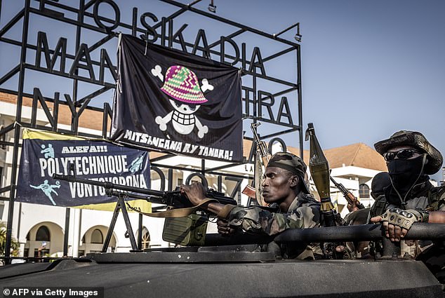 Madagascan troops ride past a large banner featuring a Malagasy version of the logo from the popular Japanese manga One Piece