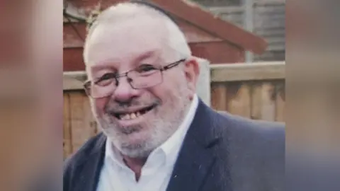 Melvin Cravitz smiles. He is wearing a dark kippah hat, glasses and a dark suit jacket with a white shirt.