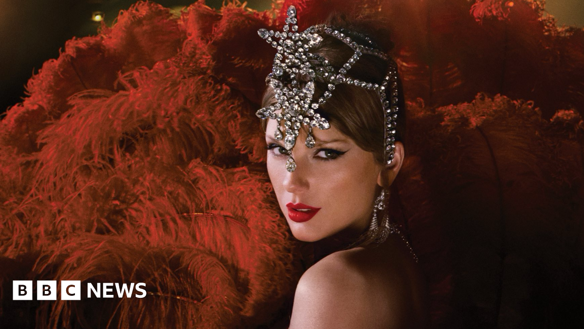 Taylor Swift is dressed as a showgirl with an elaborate, rhinestone headpiece. She is surrounded by crimson red feathers.