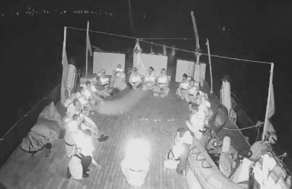 Grainy black and white image of a boat deck with people seated in a circle