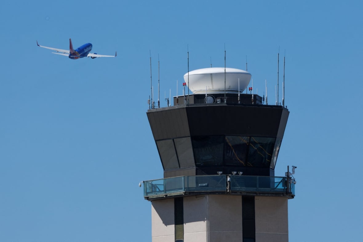 An airplane in the sky taking off next to a  big air traffic control building