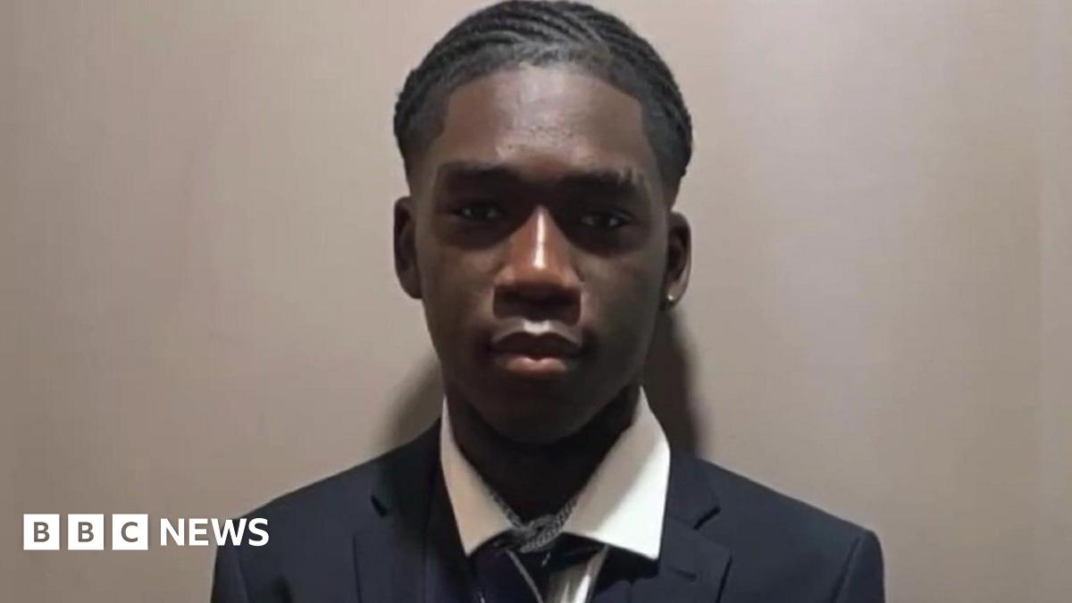 Marcus wearing school uniform blazer, shirt and tie. He is standing against a mushroom-coloured wall for a photograph.
