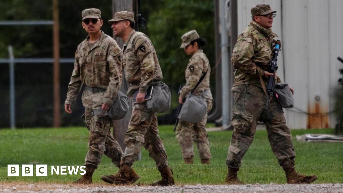Four national guard troops from Texas are wearing camouflage uniforms and walking on grass