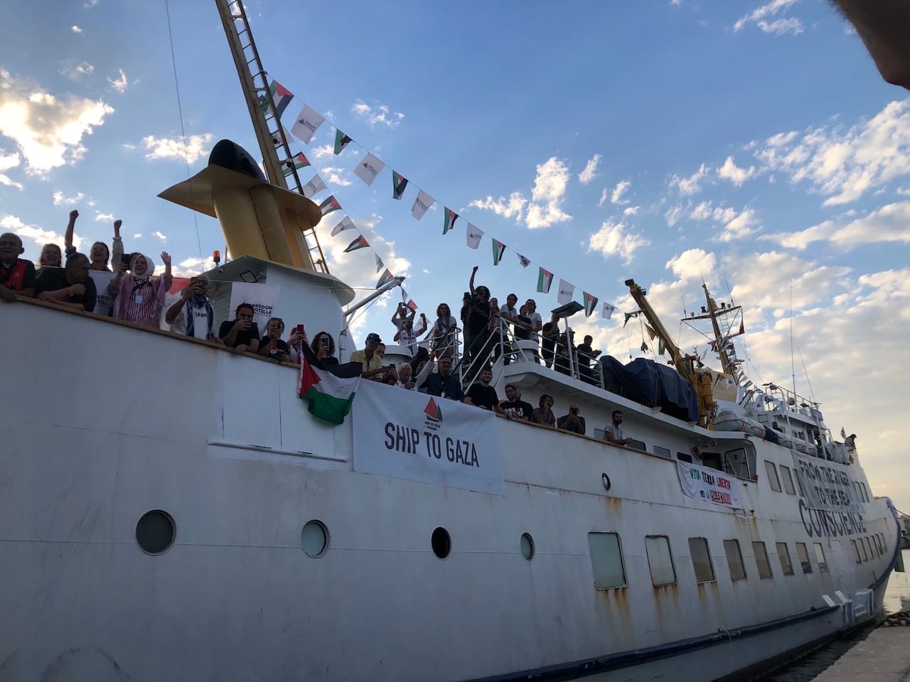 People leaning over the side of a ship, some raising their hands or waving.