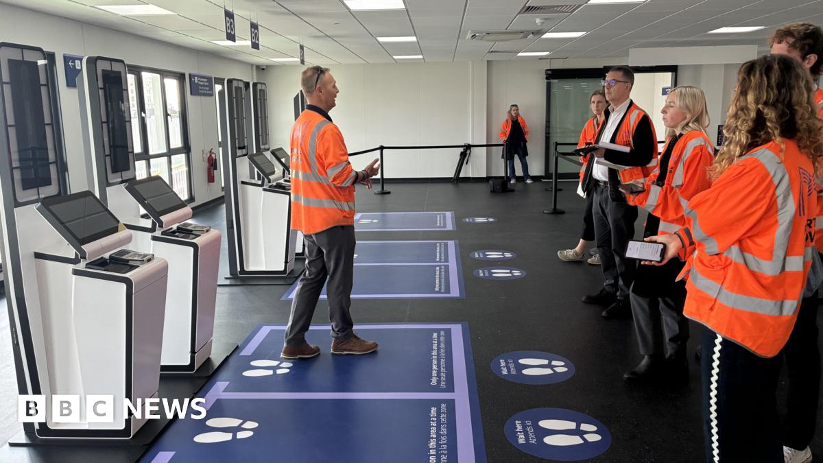 Border force staff in hi vis jackets next to finger printing terminals