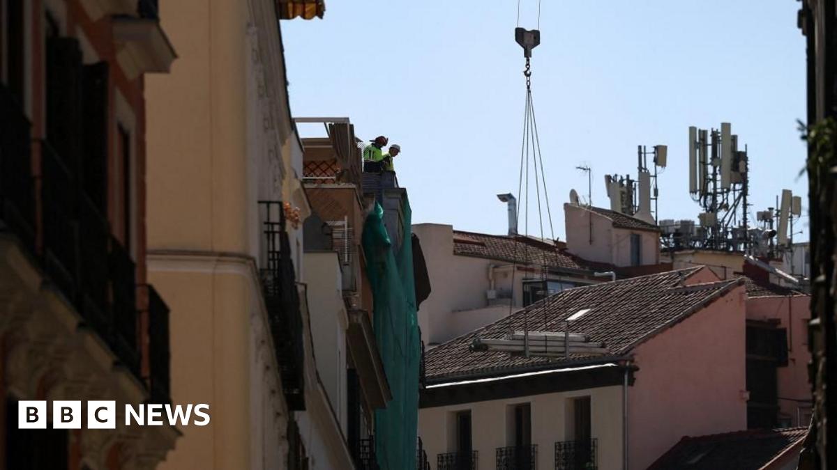 Workers stand on a building at the site of the collapse in Madrid