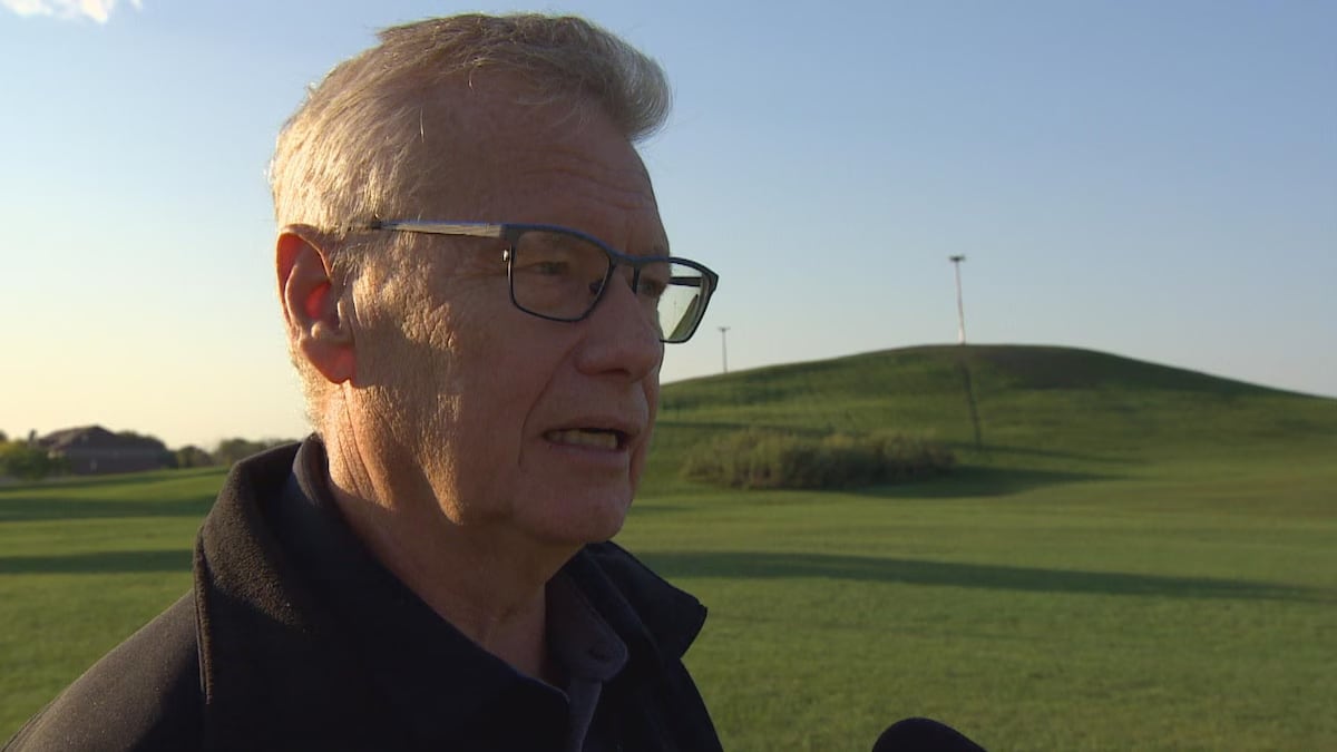 A man stands outside with a green field in the background behind him.