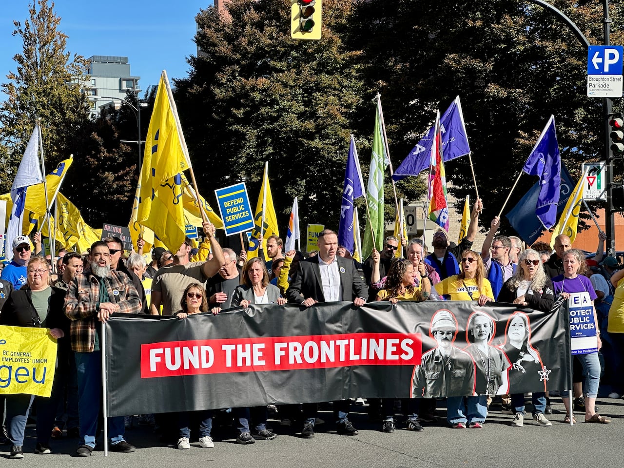 People carrying yellow and purple signs and flag, and holding a large sign that says 'fund the frontlines.'