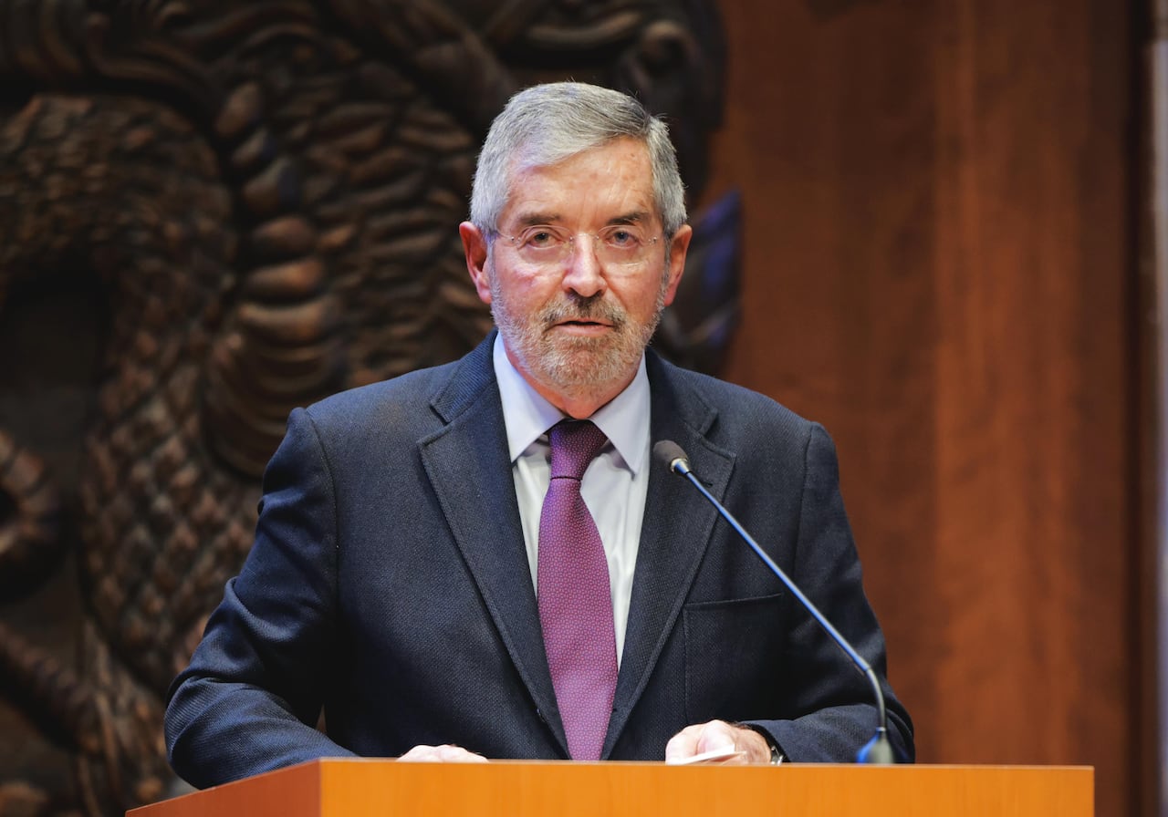 A man with glasses and wearing a suit stands behind a podium