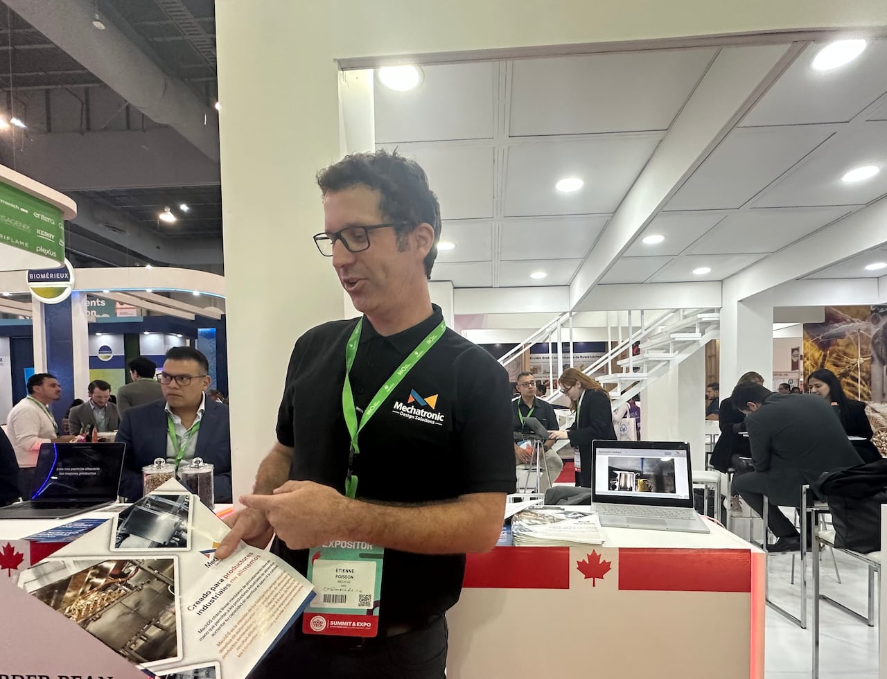 A man with glasses holds a pamphlet in a busy, well-lit area. 
