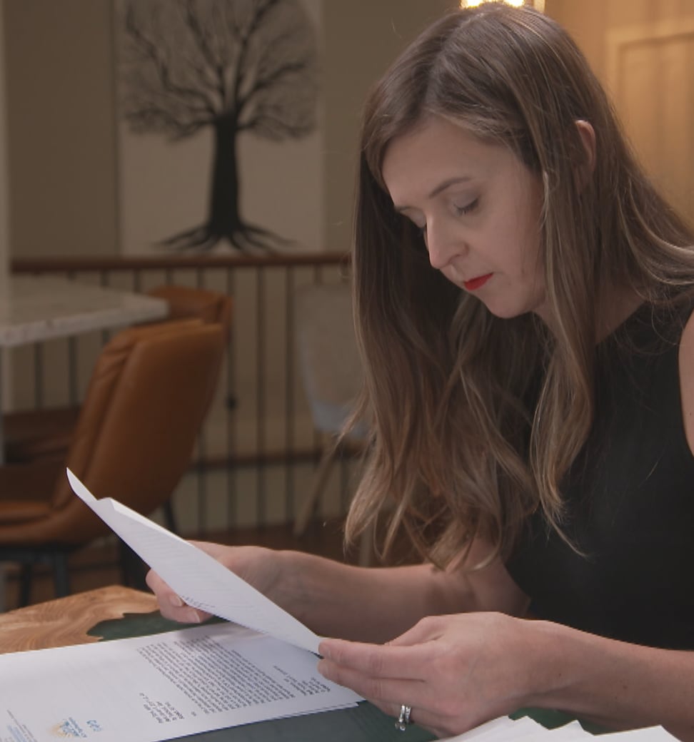 A woman sits at table and goes through documents and papers.