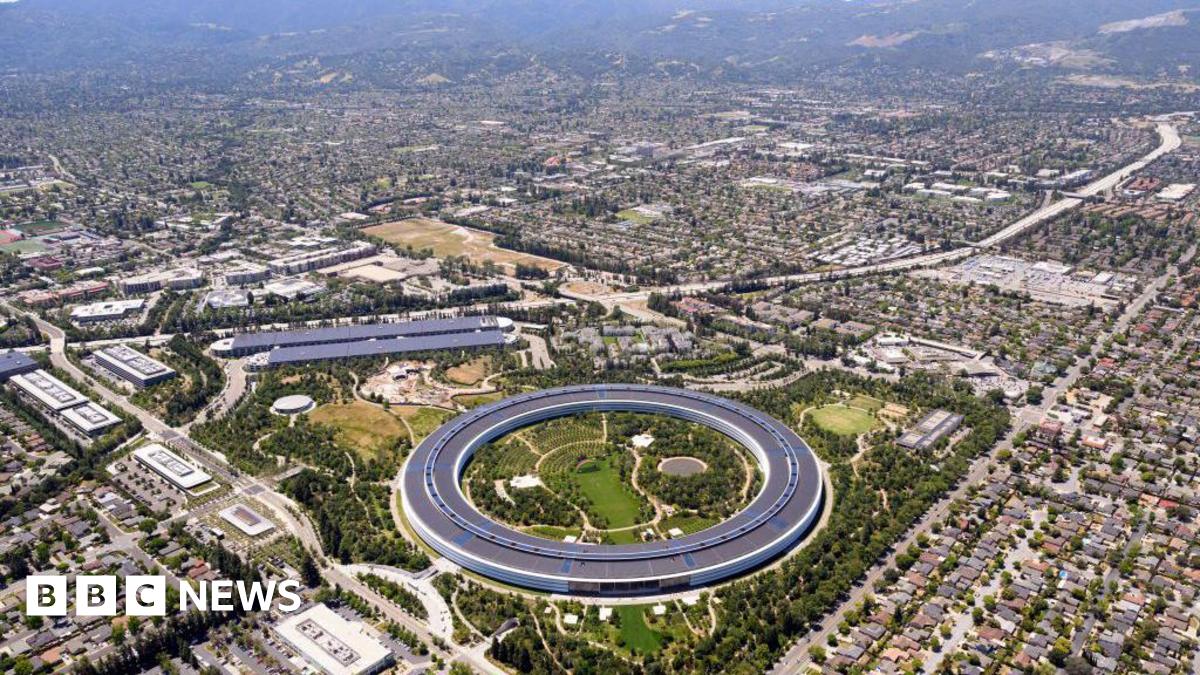 An aerial view of Silicon Valley. There are many buildings, and in the middle of the frame a large circular building in the middle of a park.