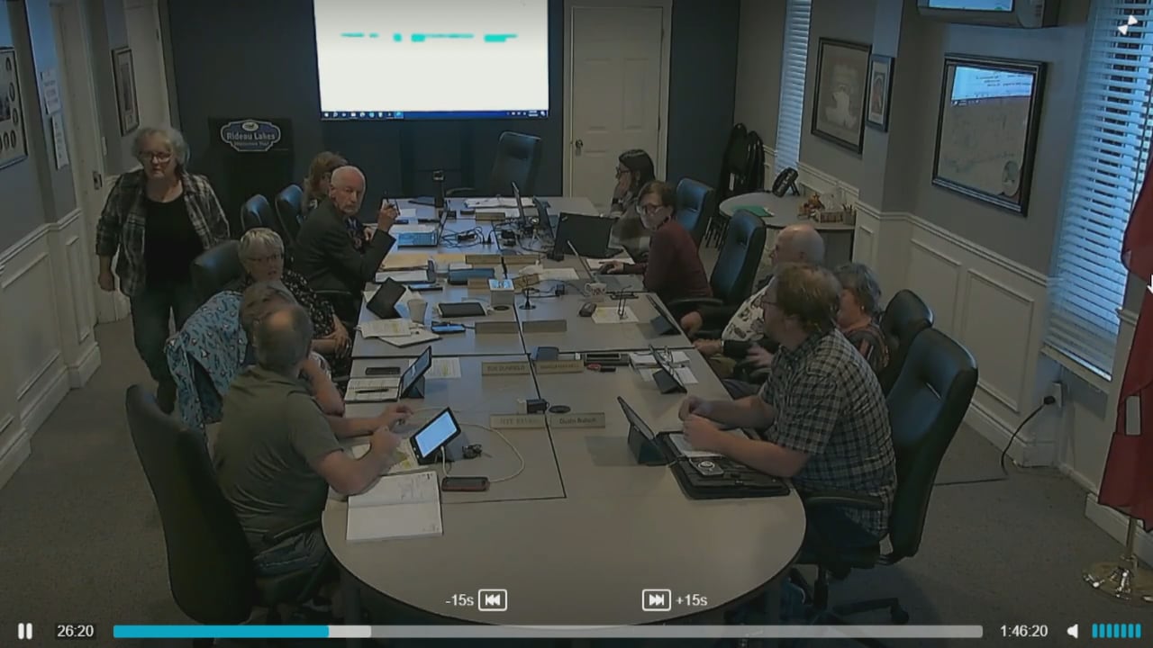 Screen grab from a council meeting. A woman is on the left side walking towards the back of the room.