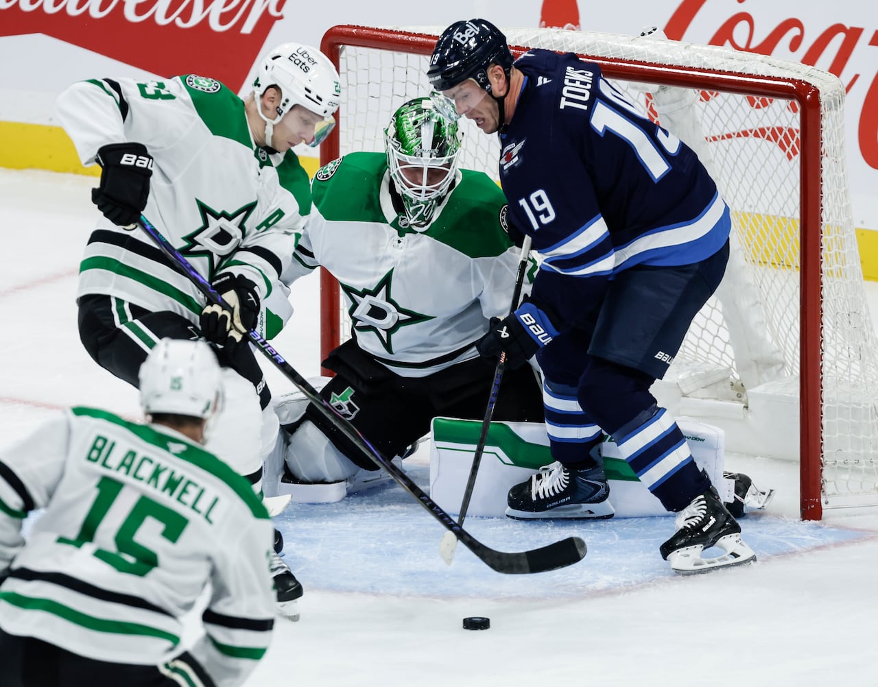 Hockey players battle for a loose puck in front of a goalie