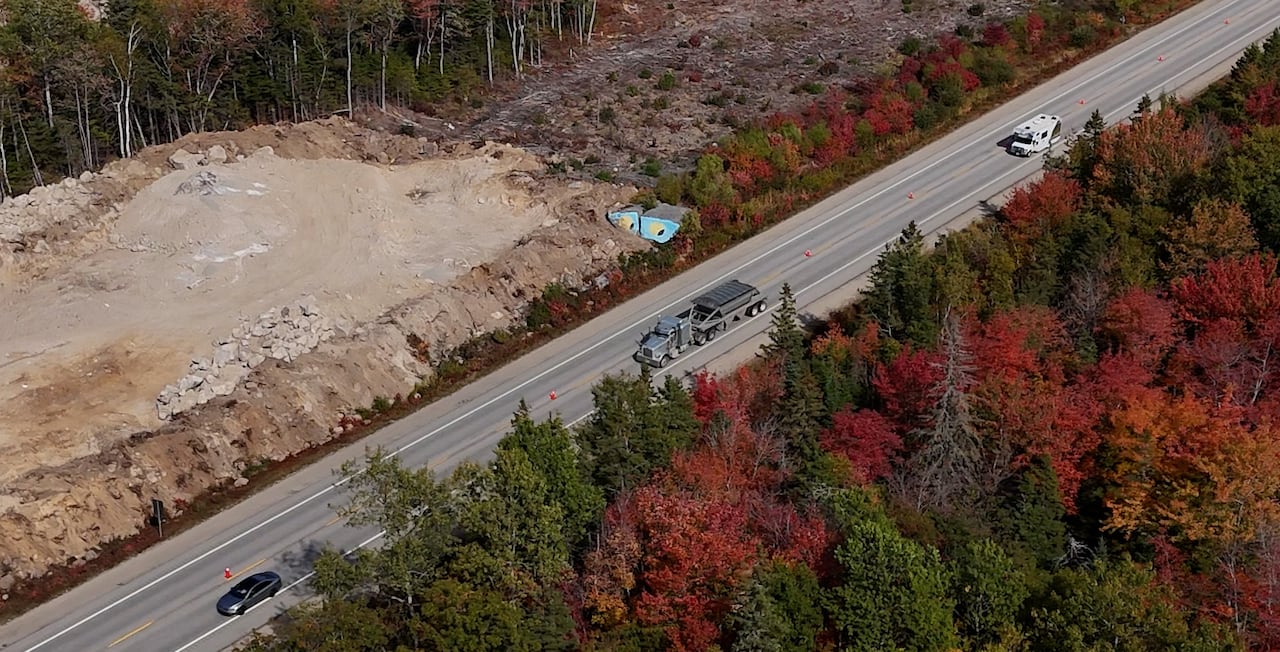 An aerial view of a highway. Next to the highway, dirt has been broken up and two large boulders painted as eyes can be seen.