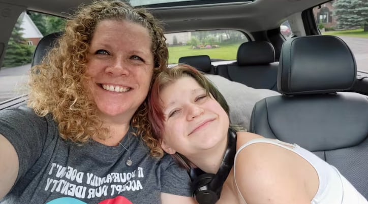 A woman and a child smile while sitting in the front seat of a car