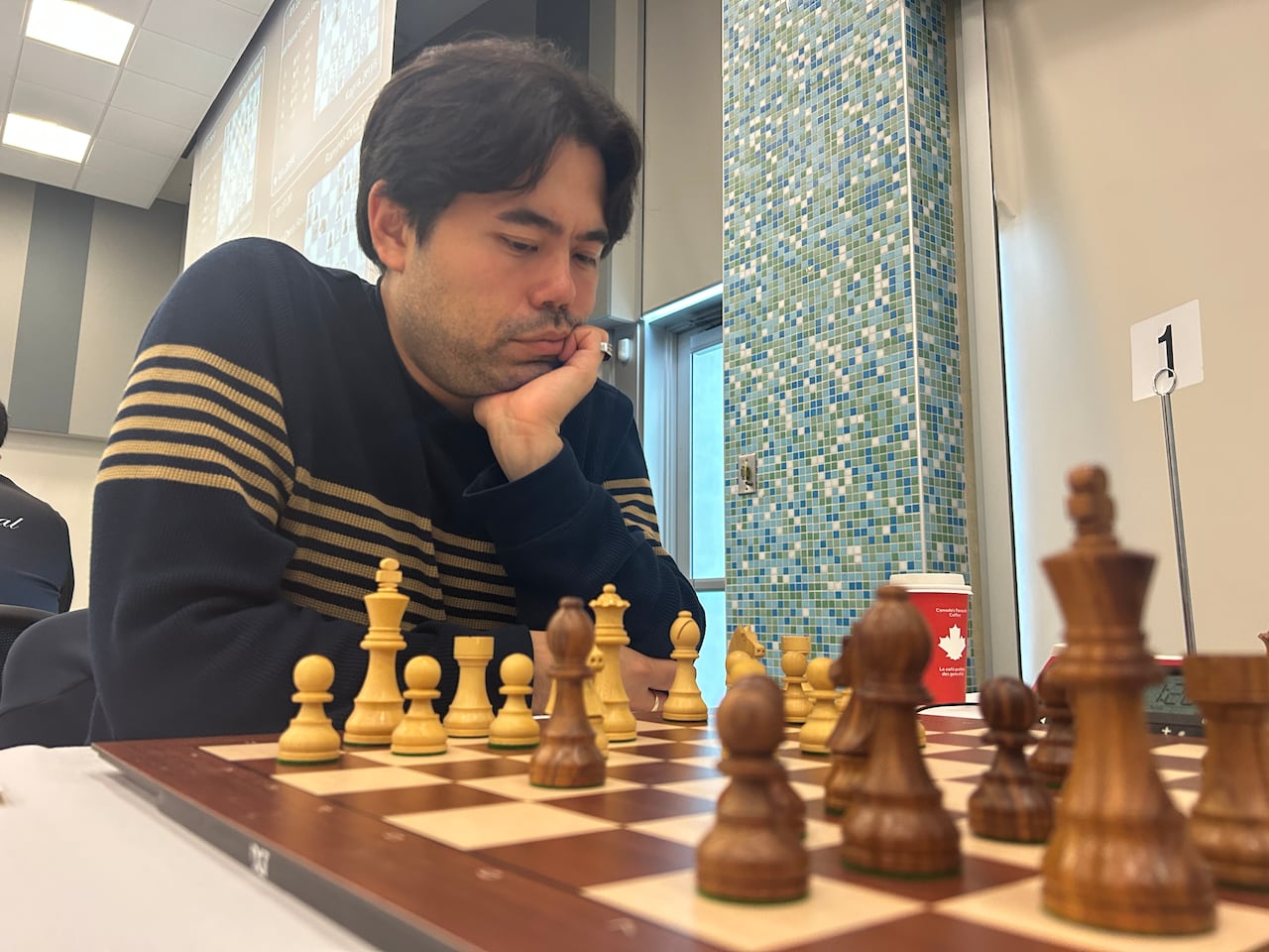 A man sits down and stares at a chess board. 