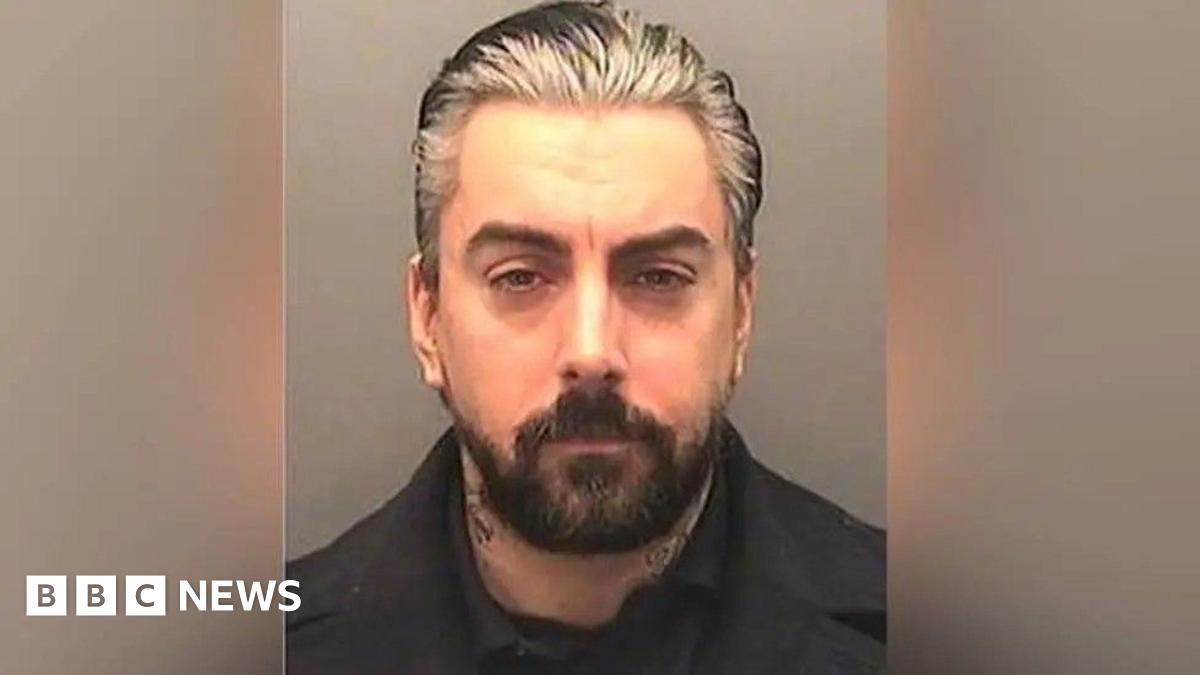 A mugshot of Ian Watkins, a man with slicked back grey hair and a short, dark-haired beard.