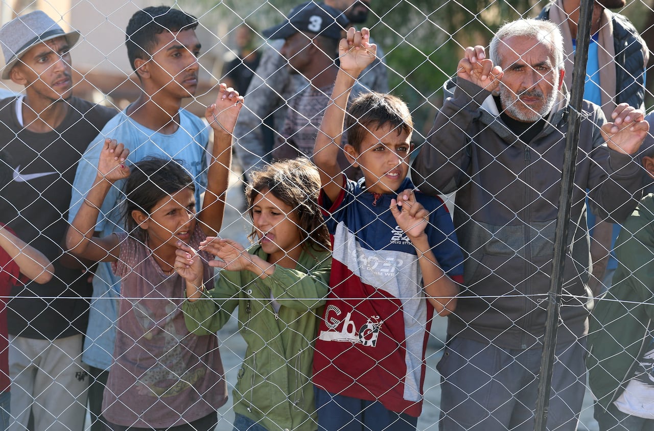 Children and a man lean against a fence.