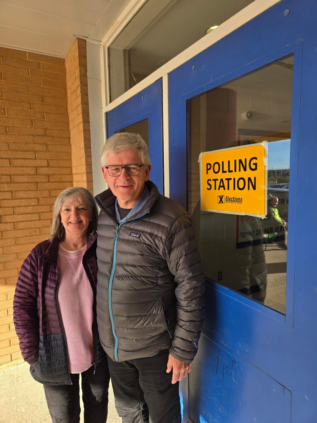 Older man and woman smile for photo outside polling station