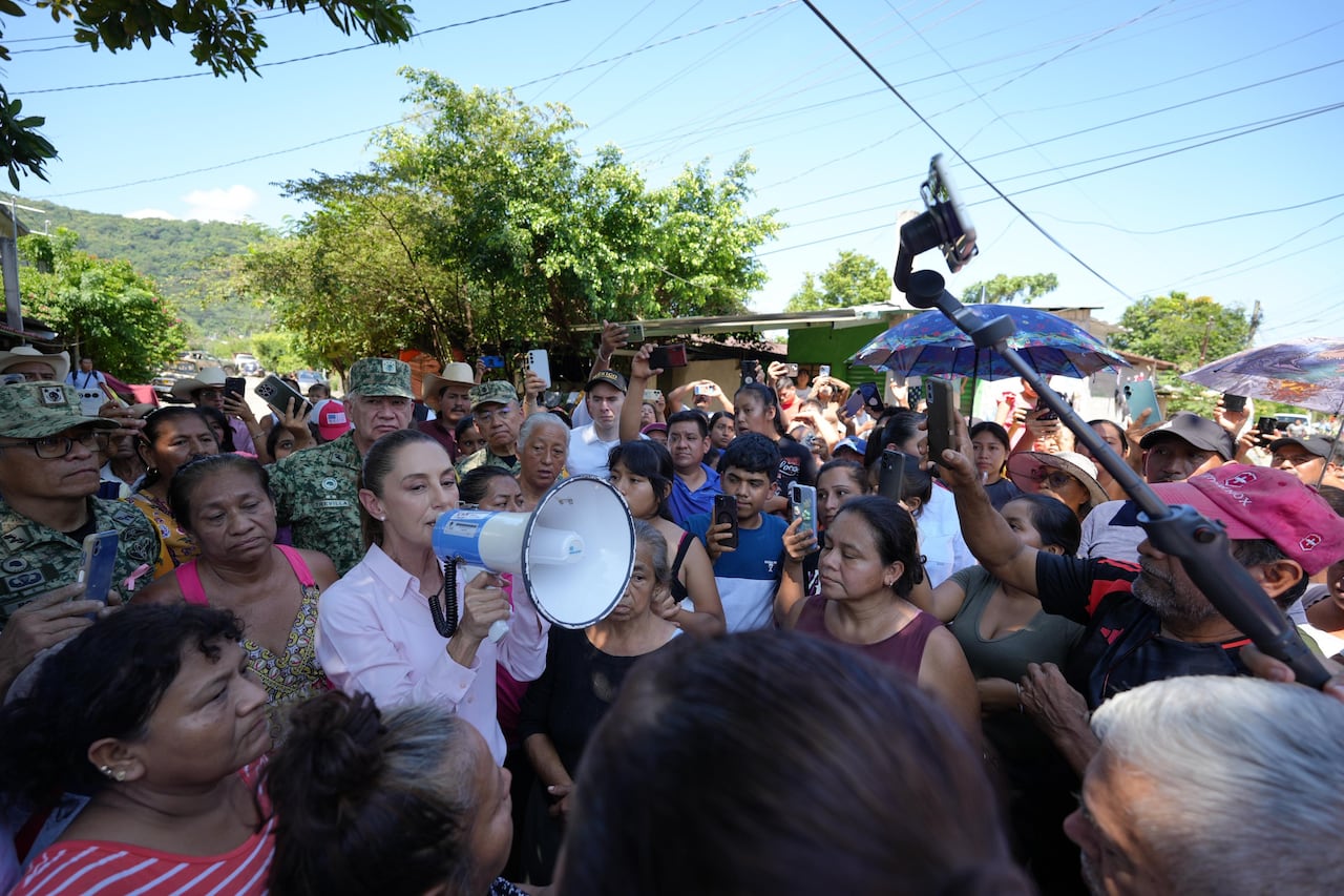 A woman with a megaphone speaks while she is surrounded by a crowd of people.