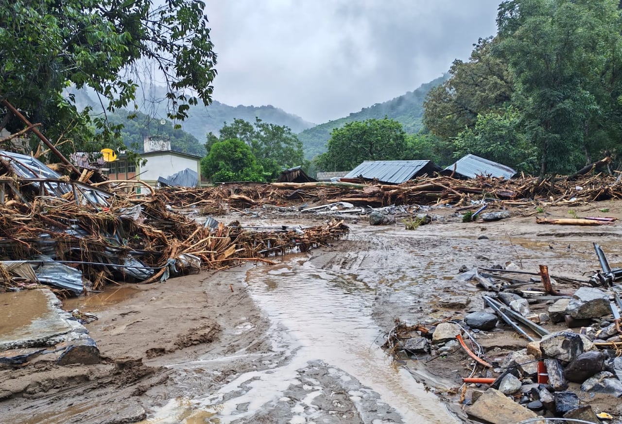 A mess of mud and debris in the foreground and the tin roofs of houses in the background.