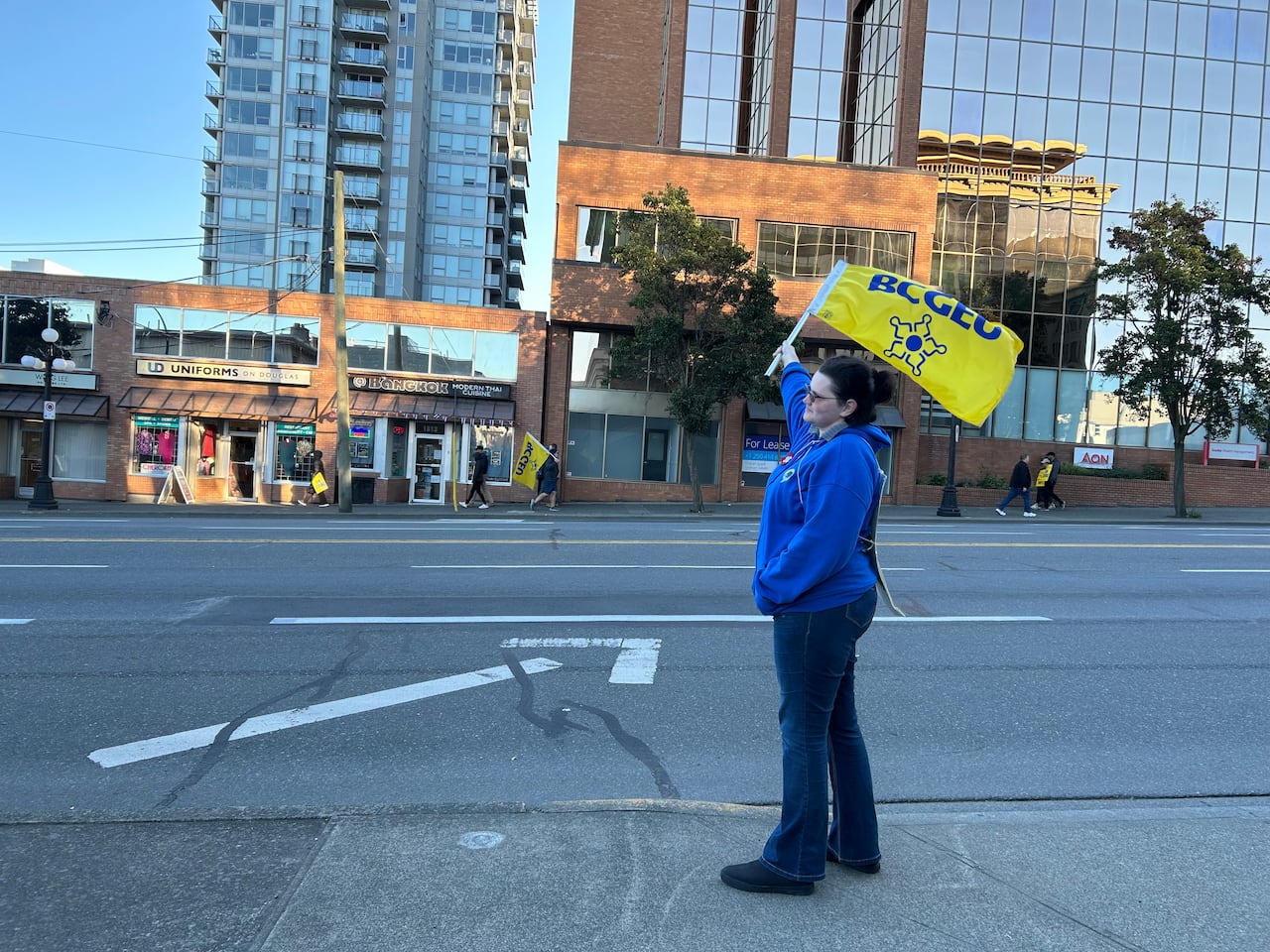 a woman stands on the side of the road with a BCGEU flag