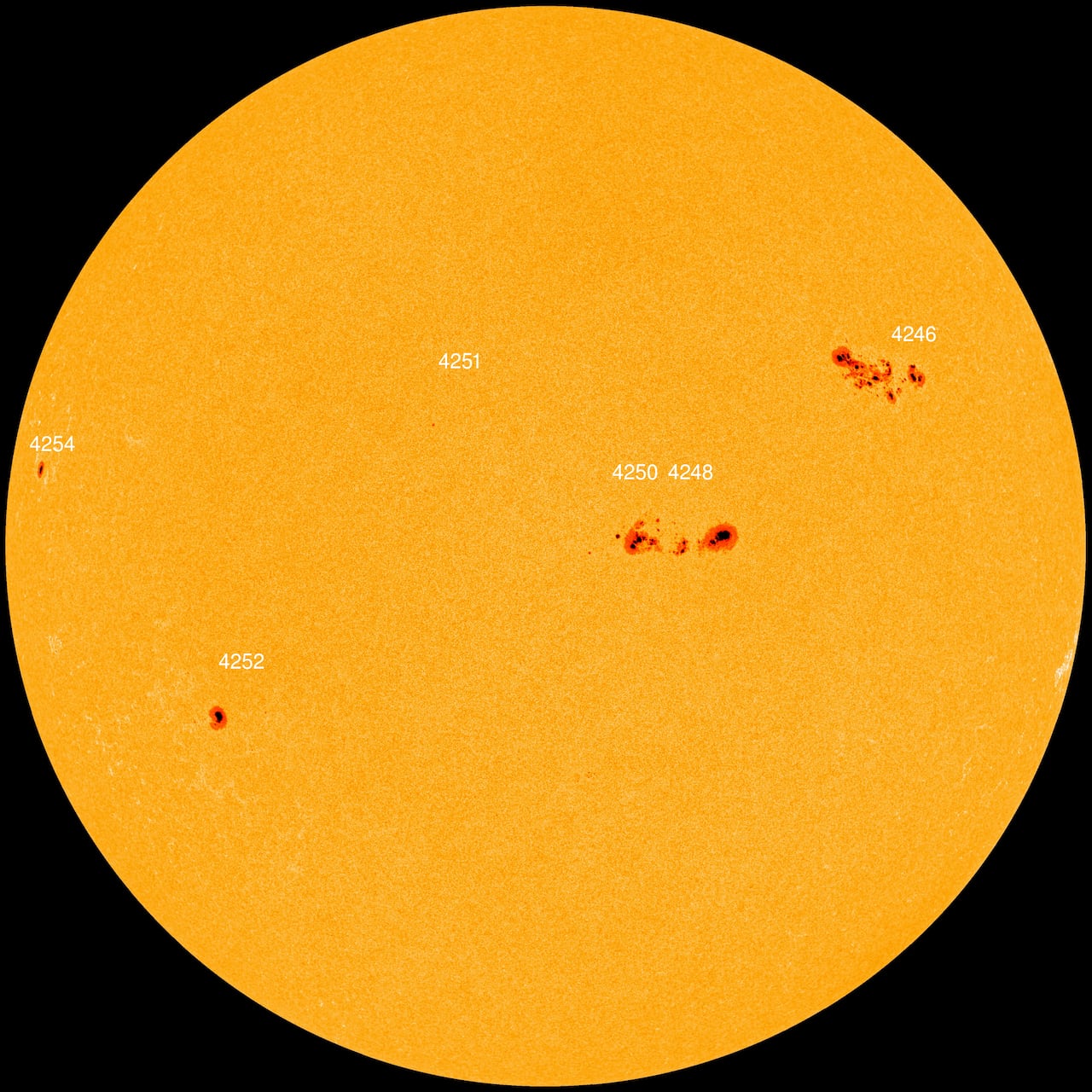 The orange disk of the sun is dotted with several dark regions.