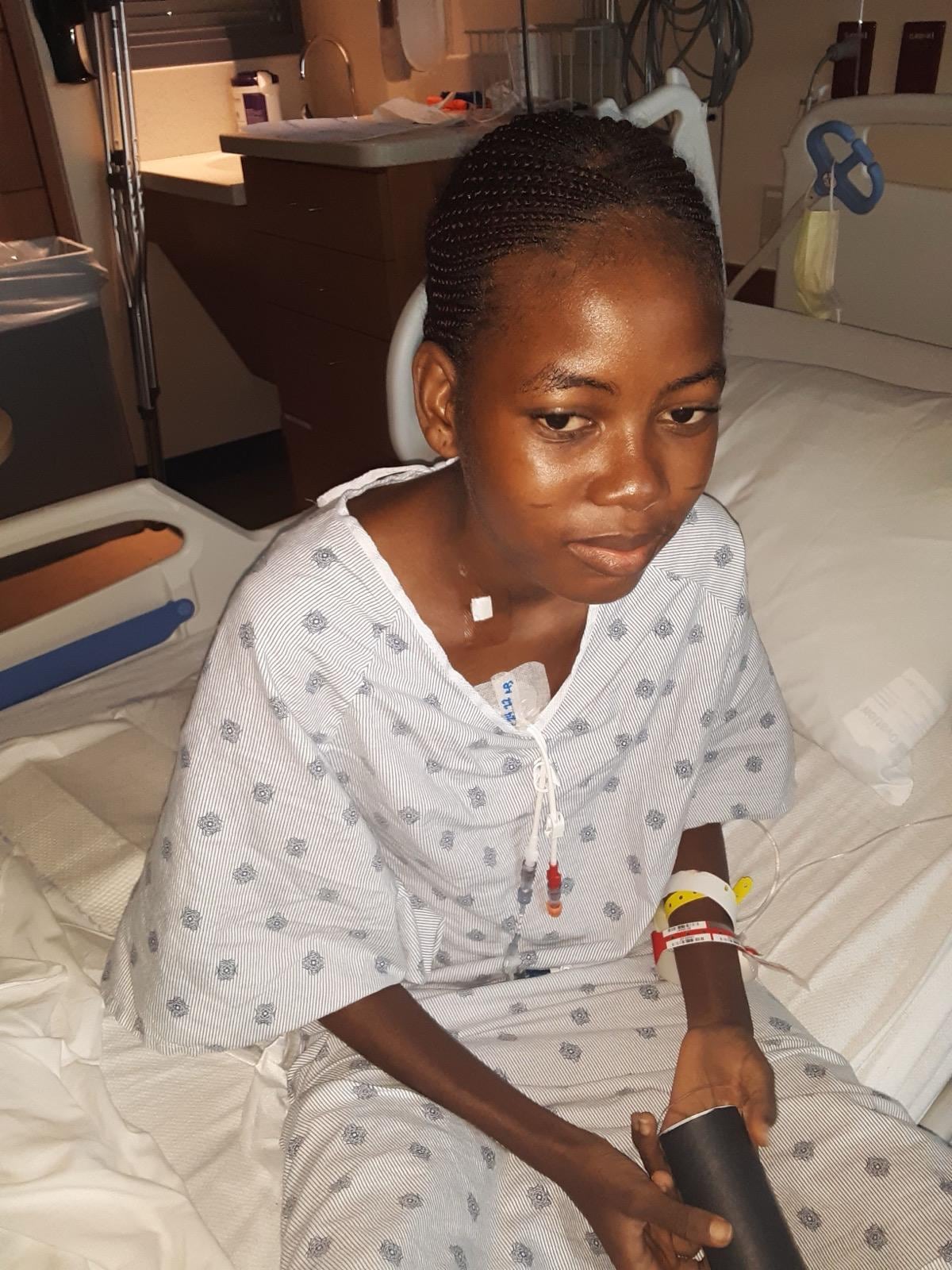 Girl in hospital robe sits on hospital bed.