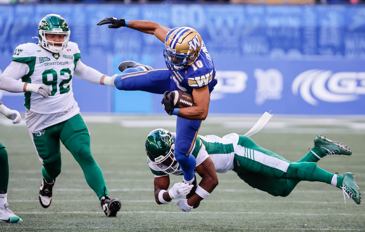 A man in a blue and gold uniform with the Number 10 flies headfirst toward the camera, a football clutched under his left arm, while a player in green and white, flying toward the left, tries to wrap his arms around his right leg.