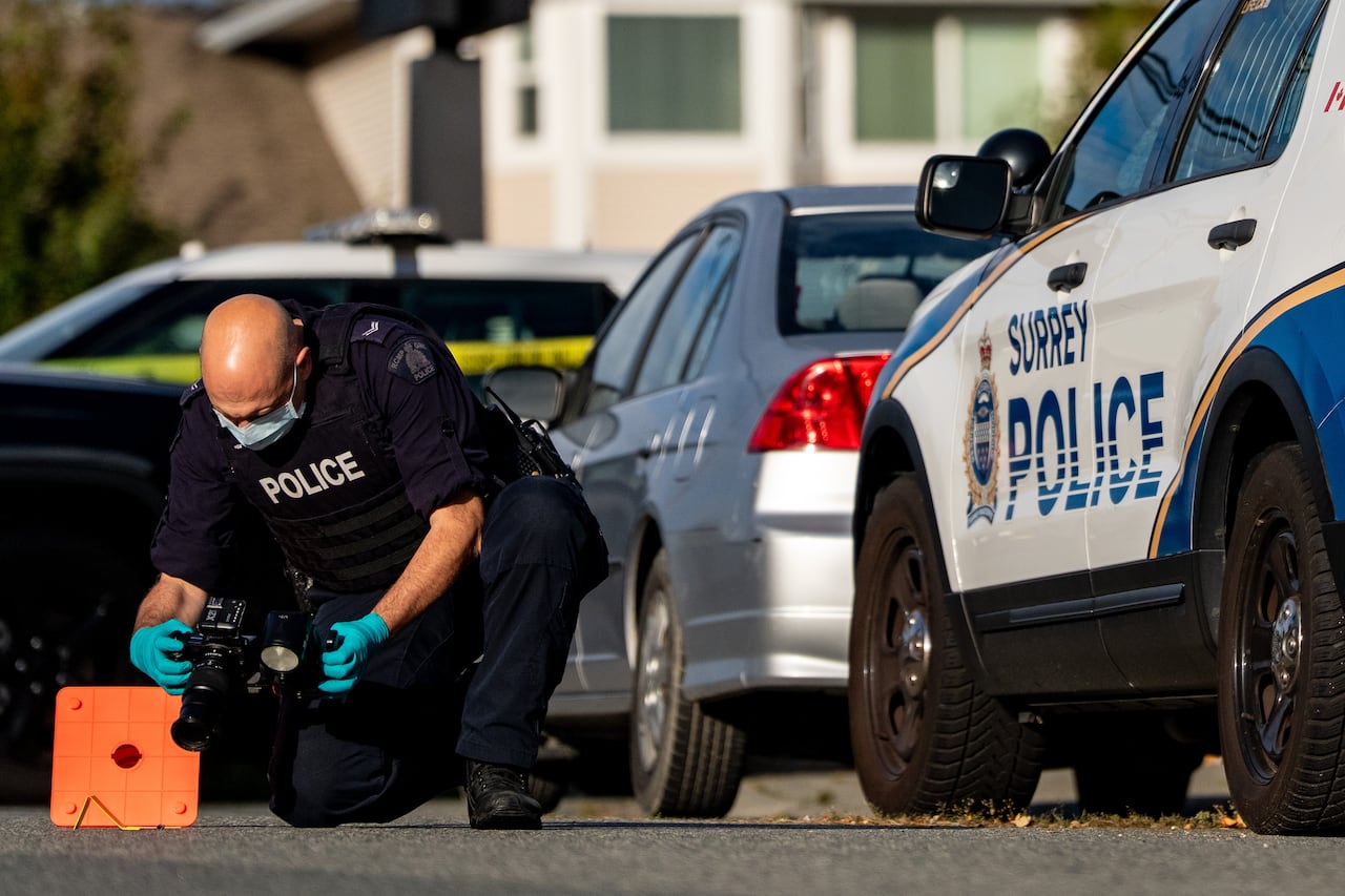 A police man crouches down taking photographs from a crime scene. 