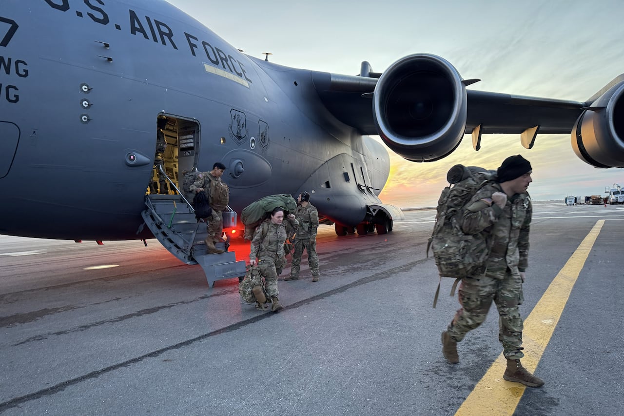 Soldiers dressed in fatigues and carrying gear walking off a U.S. Air Force plane.