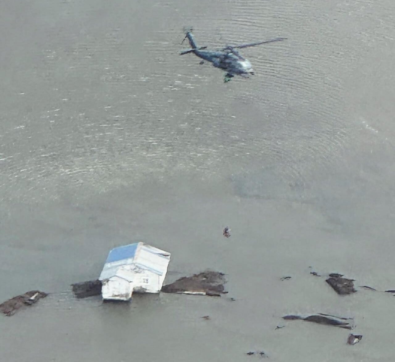 A helicopter is seen from above, over a home surrounded by floodwaters.